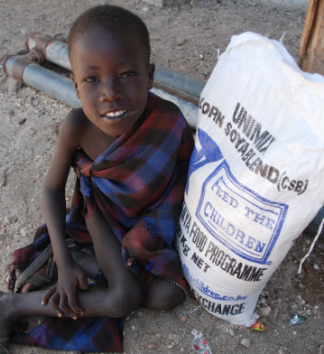 Un niño sentado al aire libre junto a una bolsa de comida