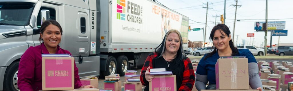 Tres mujeres de pie con cajas en un evento al aire libre