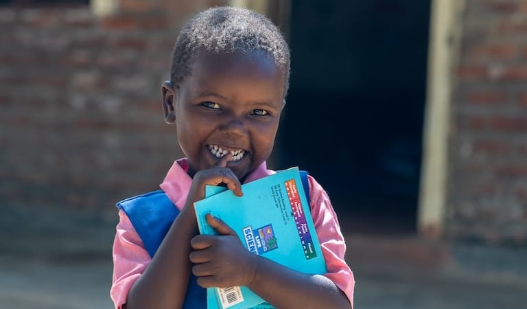 Un niño de pie al aire libre con un libro en la mano y sonriendo