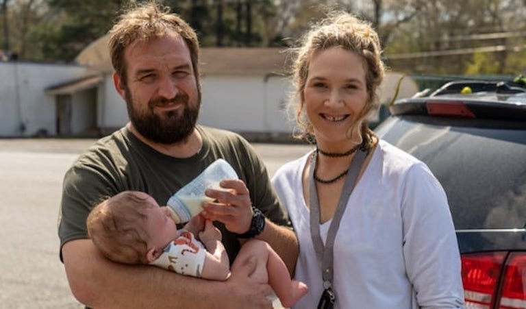 Dos personas sostienen y alimentan a un bebé al aire libre