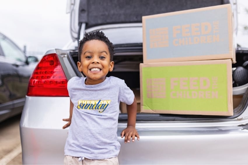 Un niño sonriendo delante de un coche con una caja dentro