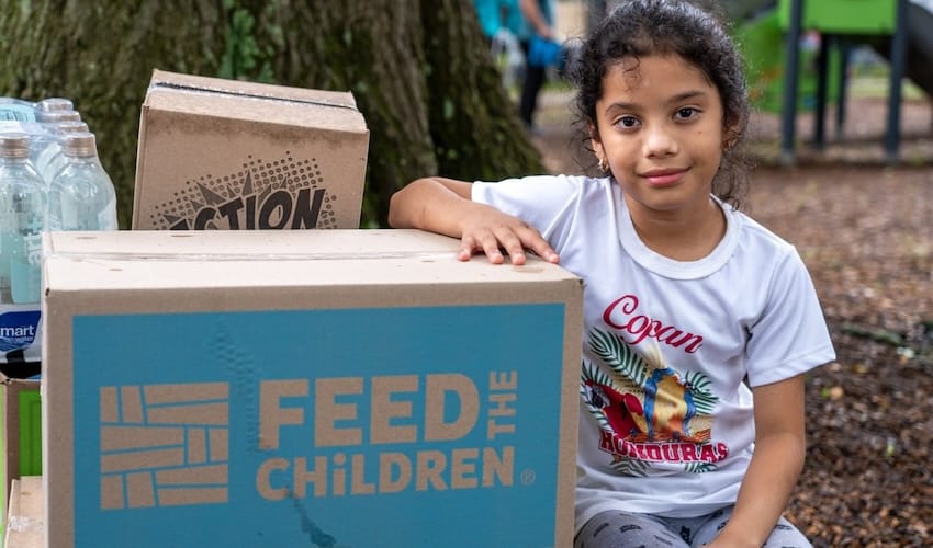 Una niña con el brazo sobre las cajas de Feed the Children al aire libre