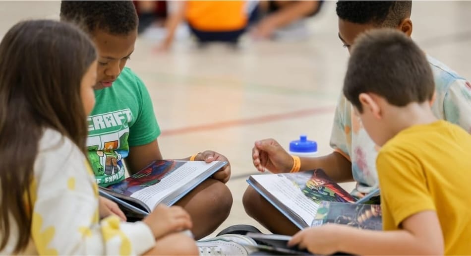 Niños reunidos leyendo libros en el gimnasio de una escuela