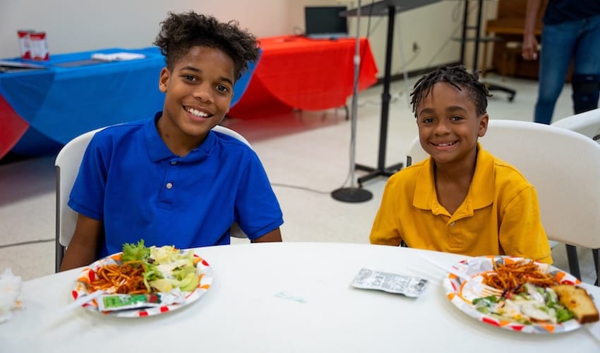 Dos chicos sentados a una mesa con comida en platos delante de ellos.