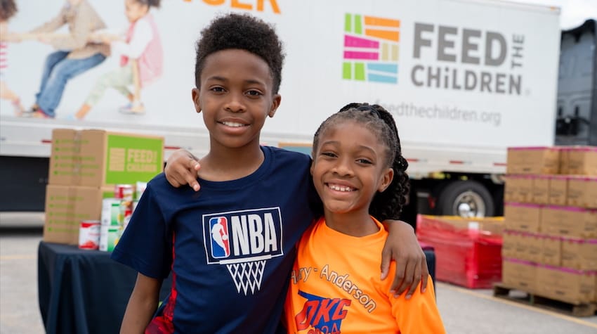 Dos niños se abrazan en un acto al aire libre con cajas