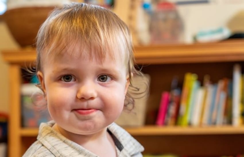 A boy looking at the camera with a bookshelf behind him.