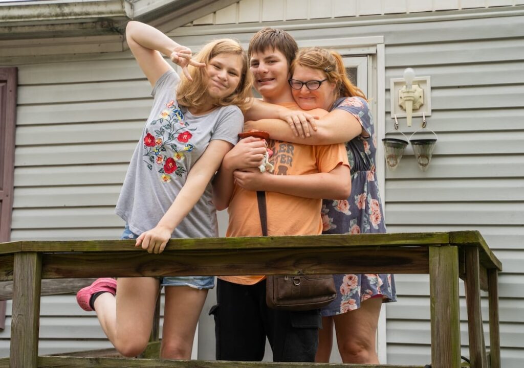 A mother, daughter, and son standing on the front porch of a house