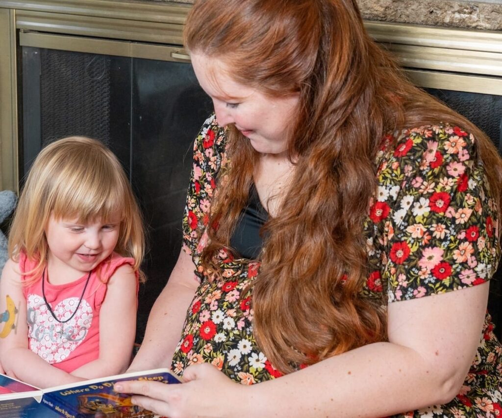 A woman and daughter reading a book together in front of a fireplace