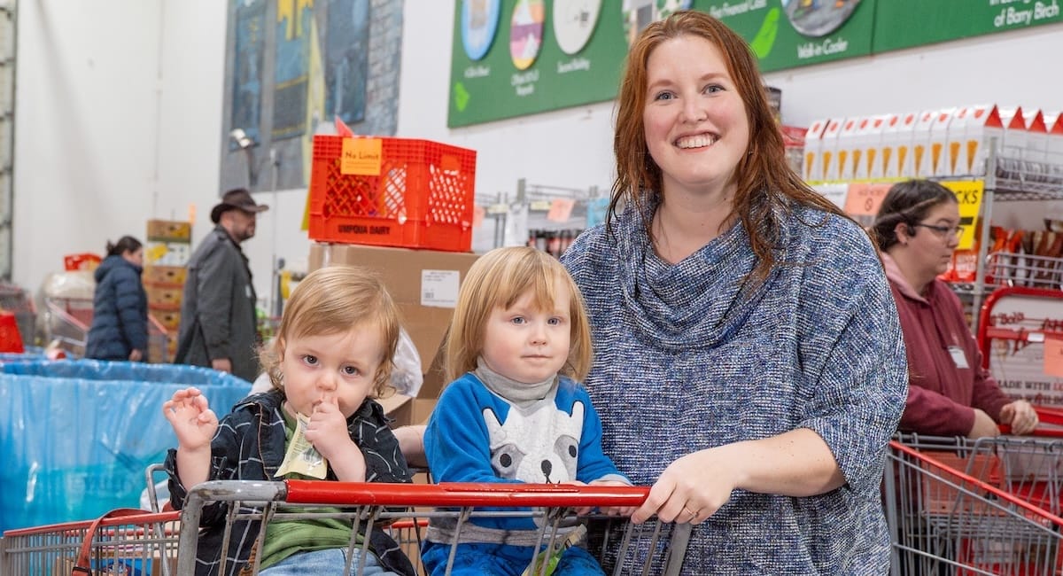 A woman and two children with a shopping cart inside of a warehouse