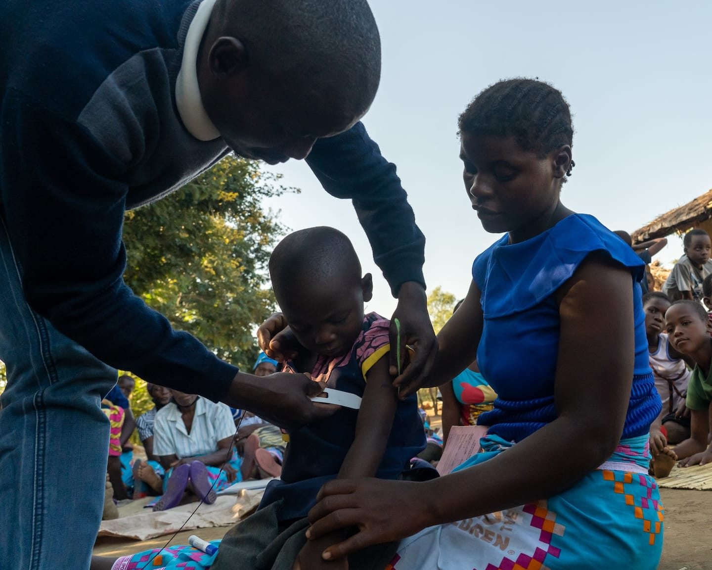 A child sitting in the lap of a woman with a man checking on the child.