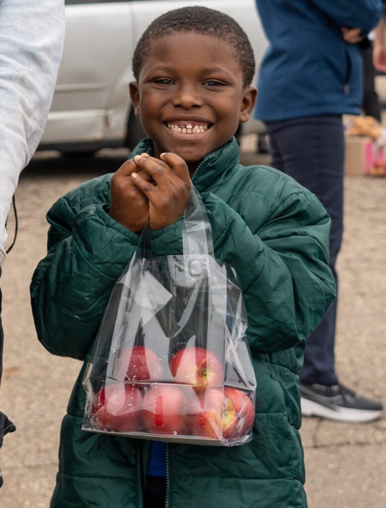 A child holding a bag of apples at an outdoor event.