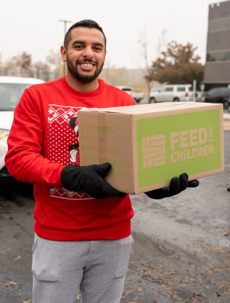 Un hombre sostiene una caja de Feed the Children en un acto al aire libre.