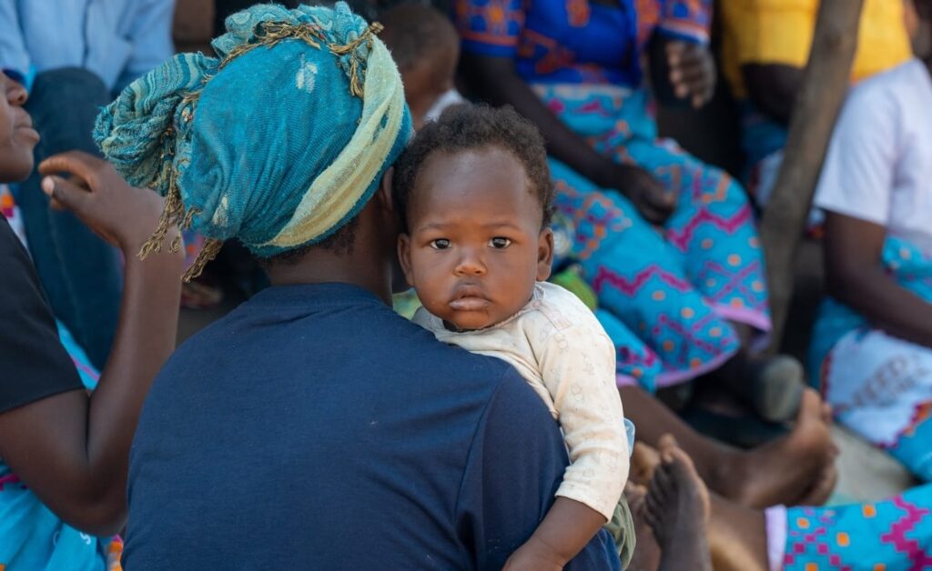 A baby being held by a woman in a crowd of people.
