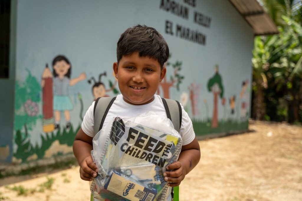 Un niño con una bolsa de Feed the Children en el exterior de una escuela.