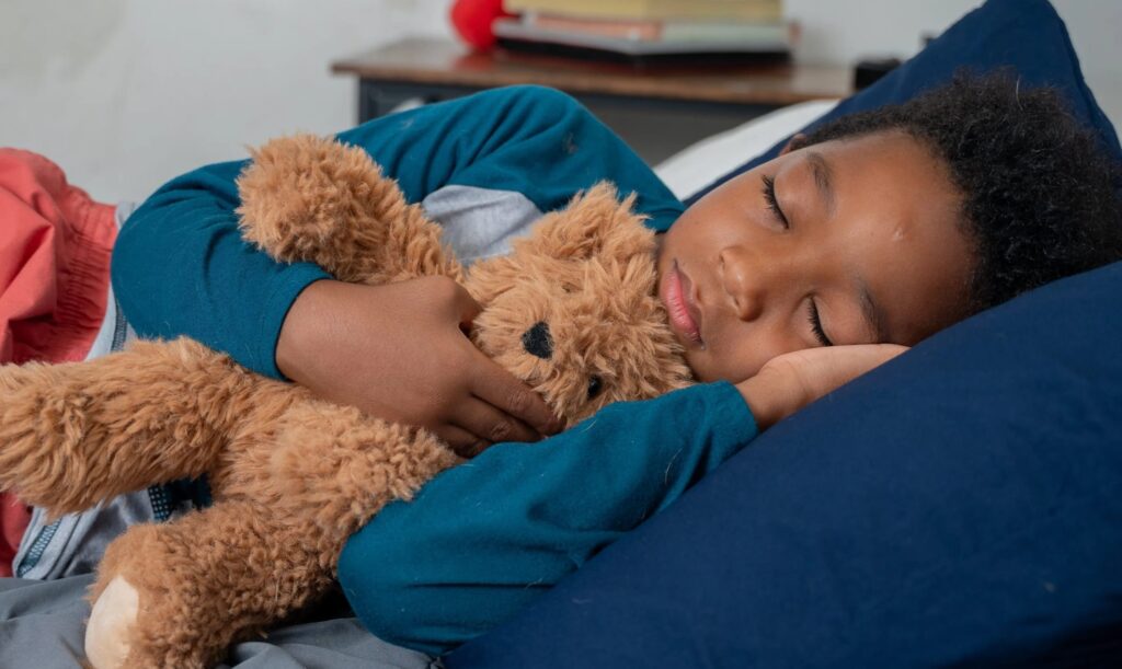 Un niño durmiendo en la cama con un osito de peluche.