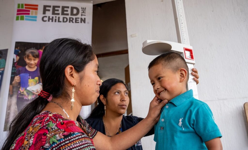 Two adults measuring the height of a child in central america.