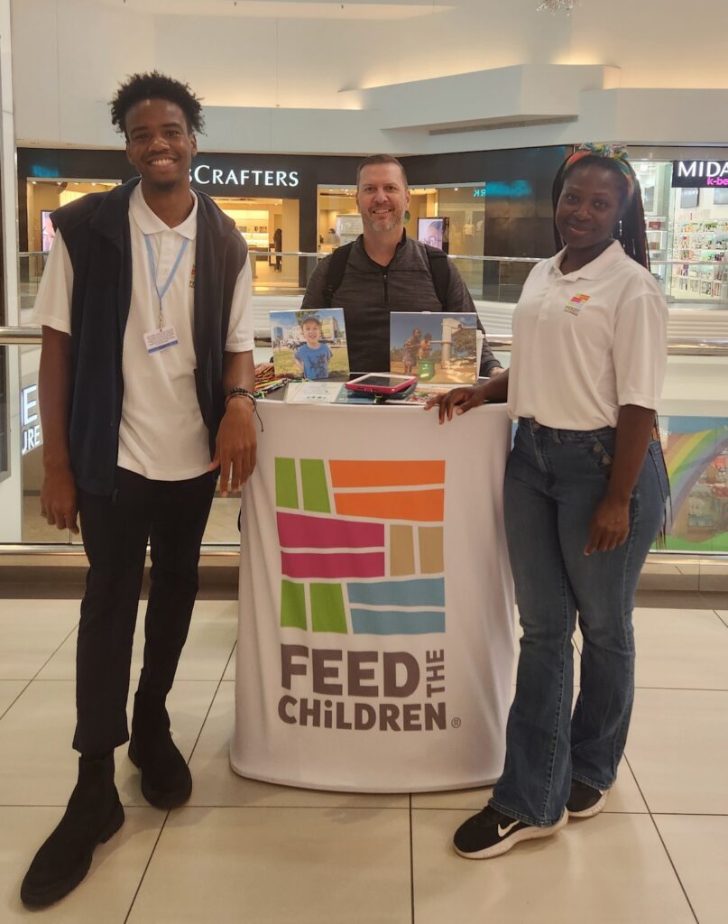 Three people standing next to a booth in a mall.