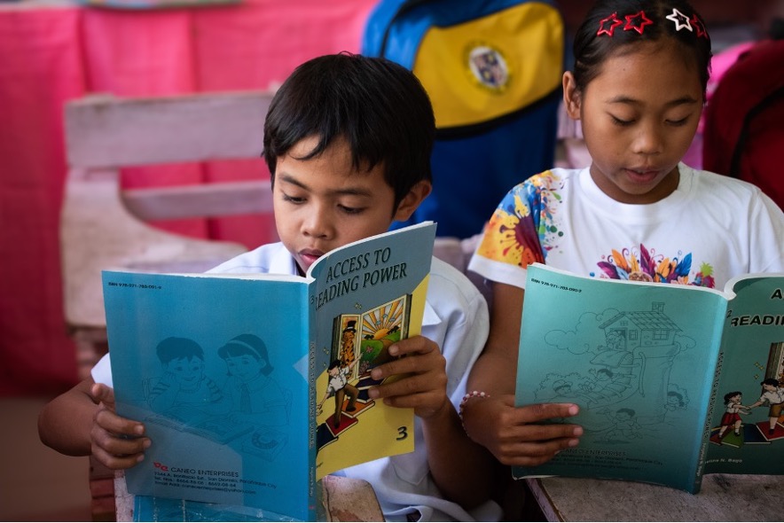 Un niño y una niña leyendo libros en la escuela.