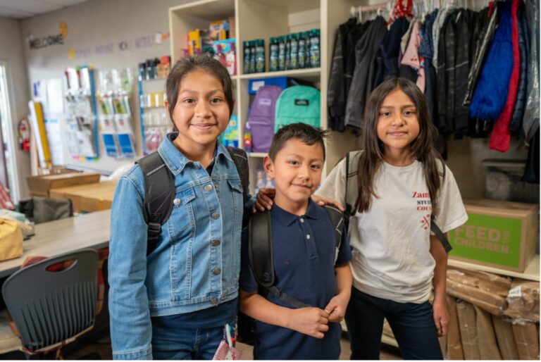 Tres niños de pie en un salón de clases.