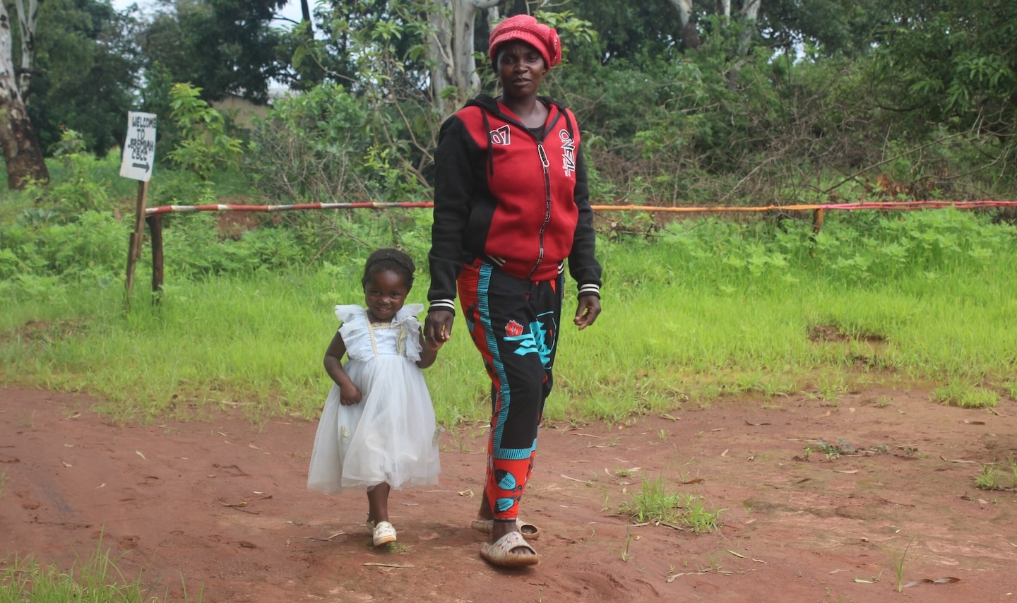 Catherine and Ackness walking in the dirt in front of the woods.