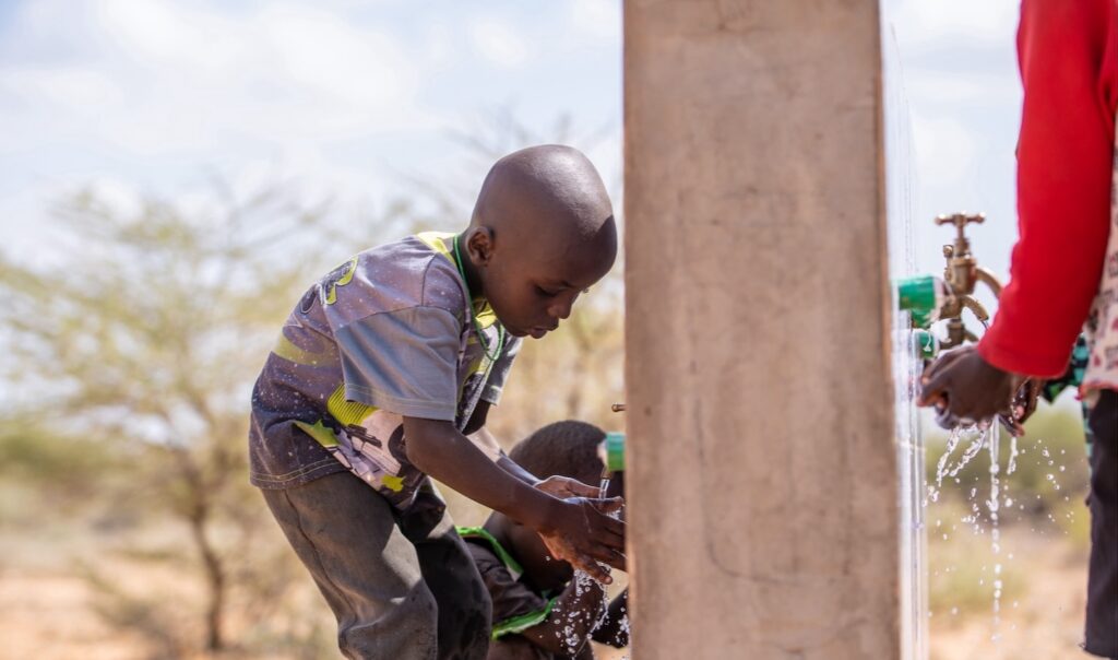 A child washing their hands in the water outdoors.