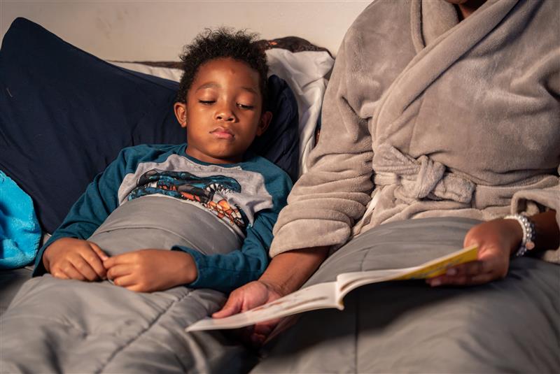 Un niño acostado en la cama junto a uno de sus padres.