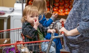 Children riding in a shopping cart in a grocery store.